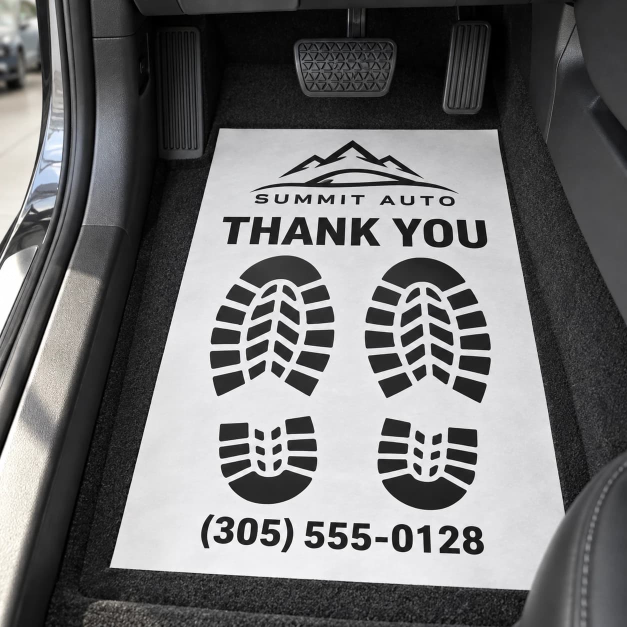 Black and white paper floor mat with fictional dealer logo above the footprints and phone below