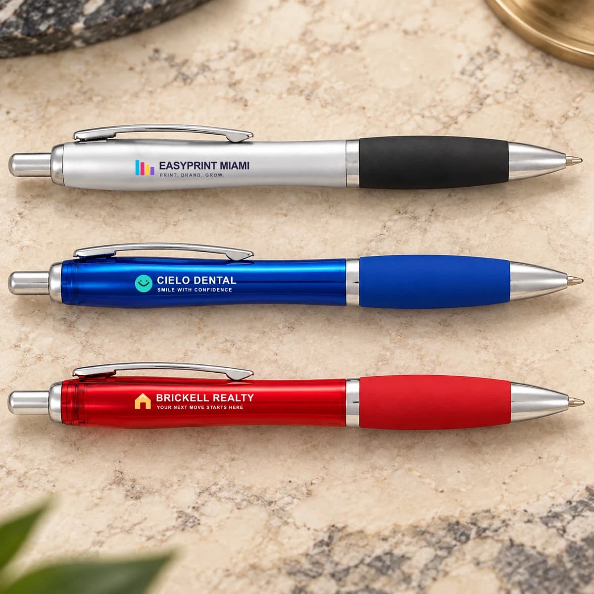 Close-up of retractable pens with full-color commercial branding on silver, blue and red barrels